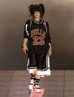 a woman with black hair wearing a basketball uniform and sneakers on the catwalk in front of a gray wall