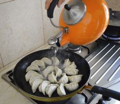 someone is cooking dumplings in a skillet on the stove with an orange kettle