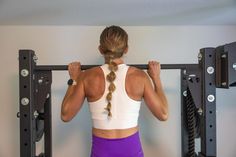 a woman in purple shorts and white tank top doing exercises on a pull up bar