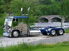 a large semi truck parked on the side of a road next to a river and bridge