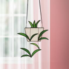 a potted plant hanging from a chain in front of a window with pink curtains