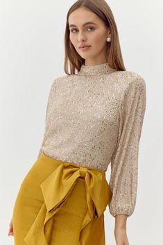 Turtleneck blouse decorated in champagne toned sequins. The back reveals a stunning exposed back with draping. Blouse Sequin High Neck Long Sleeve Length 22 1/2" Chest: 16 1/2" Waist: 14" Self: 95% Polyester 5% Spandex Lining: 95% Polyester 5% Spandex Hand wash in cold water. Dry flat. Iron on low heat. Model is wearing a size S Style #: F248T7068 Golden Top Outfit, Gold Tops For Women, Draping Blouse, Turtleneck Blouse, Knit Swimwear, Wedding Jumpsuit, Sequin Blouse, High Neck Blouse, Holiday Outfit