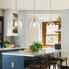 a kitchen island with stools in front of it and lights hanging from the ceiling