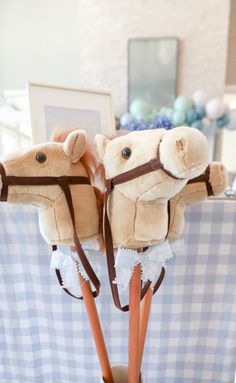 two stuffed animals on top of wooden sticks in a room with blue and white checkered table cloth