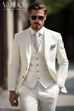 a man in a white suit and sunglasses is walking down the street with his hands in his pockets