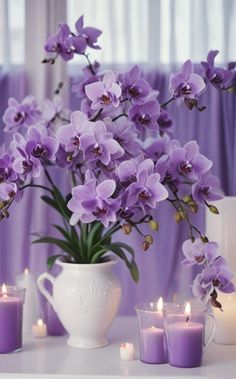 purple flowers are in a white vase on a table with candles and curtains behind it