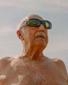 an older man with sunglasses on his face and no shirt is looking off into the distance