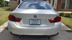 the back end of a white car parked in front of a house on a street