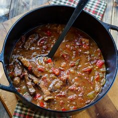 a pot filled with meat and vegetables on top of a wooden cutting board next to a knife