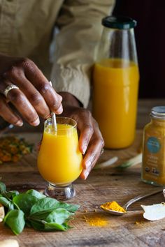 a person is pouring orange juice into a glass on a wooden table with other ingredients