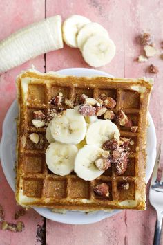 a waffle topped with bananas and walnuts on a plate next to a fork