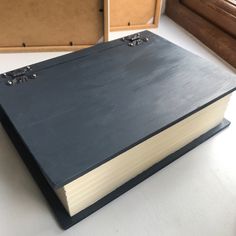 an open black book sitting on top of a table next to some boxes and drawers