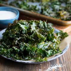 a white plate topped with kale chips next to a bowl of ranch seasoning