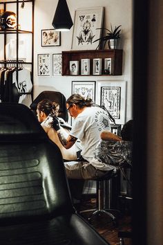 a man is getting his hair cut by another person in the room with pictures on the wall