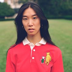 a woman in a red polo shirt is standing in the grass with her hand on her hip