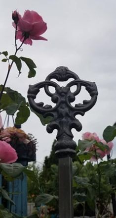 an iron cross with pink roses in the background on a cloudy day at a garden