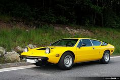 a yellow sports car is parked on the side of the road next to some rocks