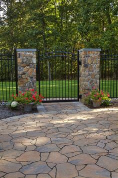 an iron gate and stone walkway leading to a lush green park