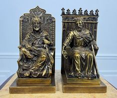 two bronze statues of king and queen sitting on thrones, one holding a book