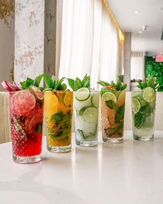 four glasses filled with different types of drinks on a table next to a white wall