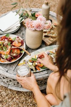 a woman sitting at a table with plates of food and flowers on the table top