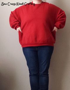 a woman standing in front of a wall with her hands on her hips wearing a red sweater