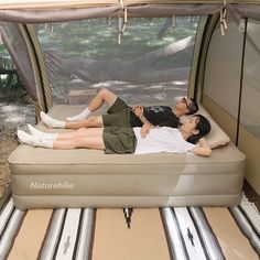 a man and woman laying on top of an inflatable bed next to a tent