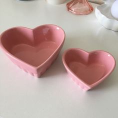 two pink heart shaped bowls sitting on top of a white table next to each other