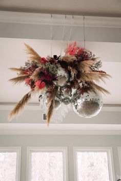 a chandelier hanging from the ceiling with feathers and flowers on it's centerpiece