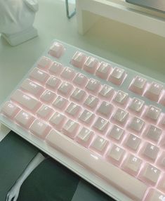 a pink computer keyboard sitting on top of a white desk next to a mouse and book