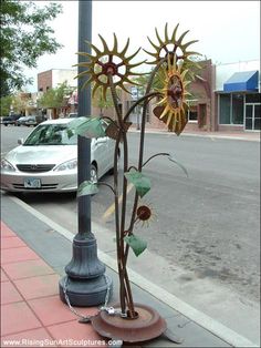 a metal sunflower sculpture on the sidewalk next to a street