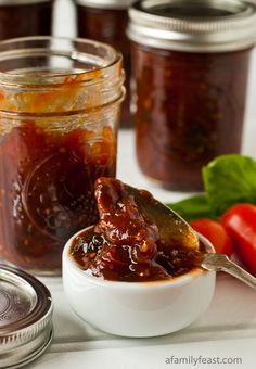 a spoon full of jam sitting on top of a table next to tomatoes and basil