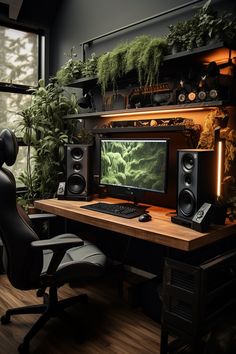 a computer desk topped with a monitor and speakers next to a plant filled wall behind it