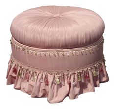 a pink round ottoman with tassels on it