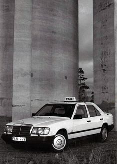 an old photo of a taxi cab parked in front of two tall concrete pillars,