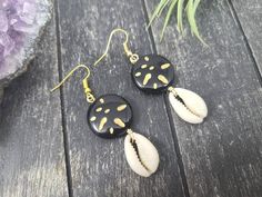 These gorgeous dangle earrings feature genuine off-white sliced moneta cowrie shells dangling beneath 20mm round carved black and gold acrylic beads an etched Afrocentric abstract pattern. Aching for acrylics? Check out the rest of my acrylic jewelry here: https://etsy.me/2IadiWZThroughout Africa and the Americas, cowrie shells have historically been viewed as symbols of womanhood, fertility, and prosperity. Check out my other cowrie shell jewelry here: https://etsy.me/2VQS0r0These earrings meas Black Round Summer Jewelry, Cowrie Shell Earrings For Gifts, Black Drop Earrings For Summer, Black Dangle Jewelry For Beach, Black Shell Jewelry For Gifts, Black Shell Jewelry Gift, Black Shell Jewelry As A Gift, Handmade Black Jewelry For Vacation, Black Shell Bohemian Jewelry