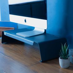 an apple computer sitting on top of a wooden desk next to a potted plant