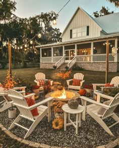 a fire pit surrounded by white chairs and pumpkins in front of a large house