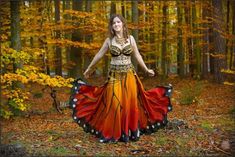 a woman is standing in the woods with a butterfly wings skirt on and her arms spread out