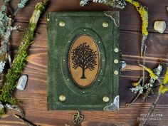 a green book with a tree on it sitting next to some branches and moss covered rocks