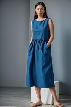 a woman wearing a blue dress standing in front of a gray wall with her hands on her hips