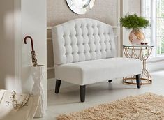 a white bench sitting in the middle of a living room next to a table with a vase on it