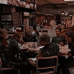 a group of people sitting around a table in a restaurant eating food and drinking beer