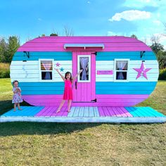 two children standing in front of a pink and blue trailer shaped like a camper