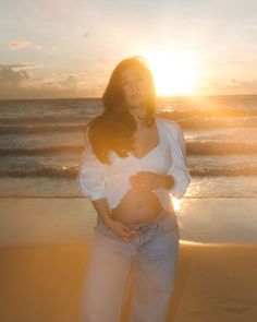 a pregnant woman standing on the beach at sunset