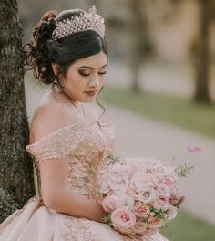 a woman wearing a tiara sitting next to a tree holding a bridal bouquet