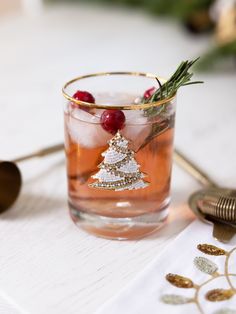 a holiday cocktail with cranberry and rosemary garnish in a glass on a white table