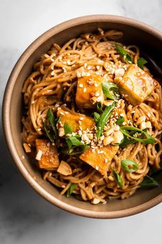 a bowl filled with noodles and tofu on top of a marble countertop next to chopsticks