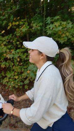 a woman holding a baby in a stroller while walking down the street with trees behind her