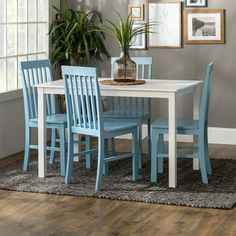 a white table with blue chairs in front of a potted plant on top of a rug